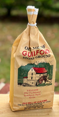 Bag of Old Mill of Guilford stone ground grits with a scenic illustration on a wooden surface.