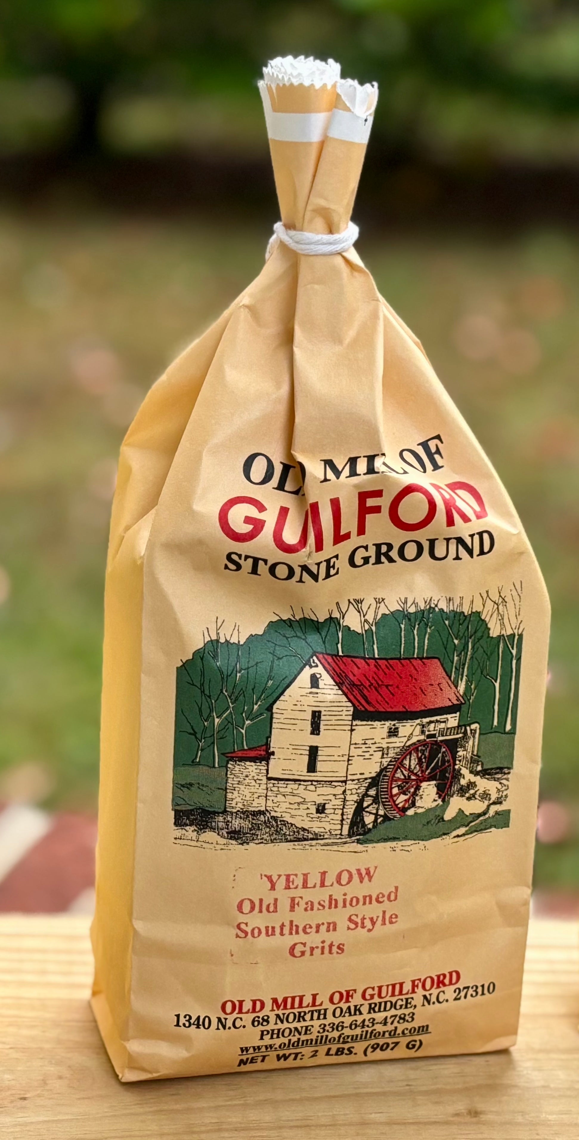 Bag of Old Mill of Guilford stone ground grits with a scenic illustration on a wooden surface.